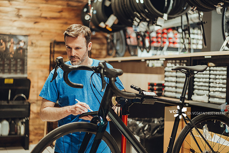 白人男性自行车修理工的肖像检查平板电脑在他的车间自行车图片素材