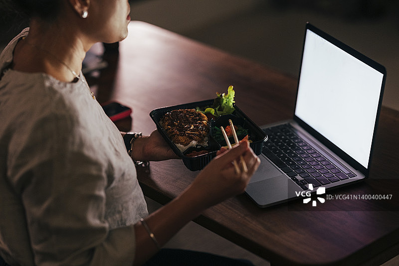 一位匿名女子一边享受美食，一边在笔记本电脑上阅读图片素材