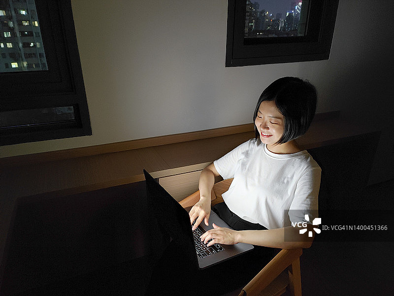 亚洲女性晚上在家用笔记本电脑工作图片素材