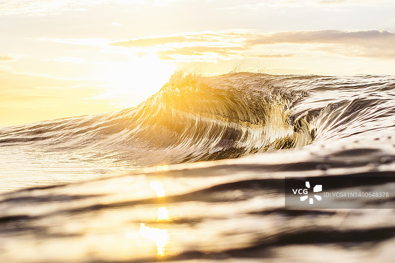 高对比度明亮的海洋波浪站在直接金色光与镜头耀斑图片素材