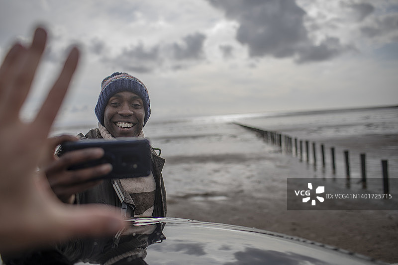 在冬季海滩上拿着手机拍照的快乐男人图片素材