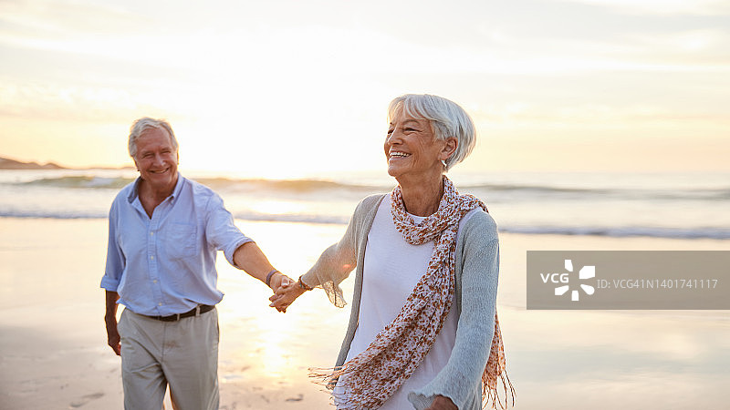 夕阳西下时，老妇人带着丈夫沿着海滩大笑图片素材