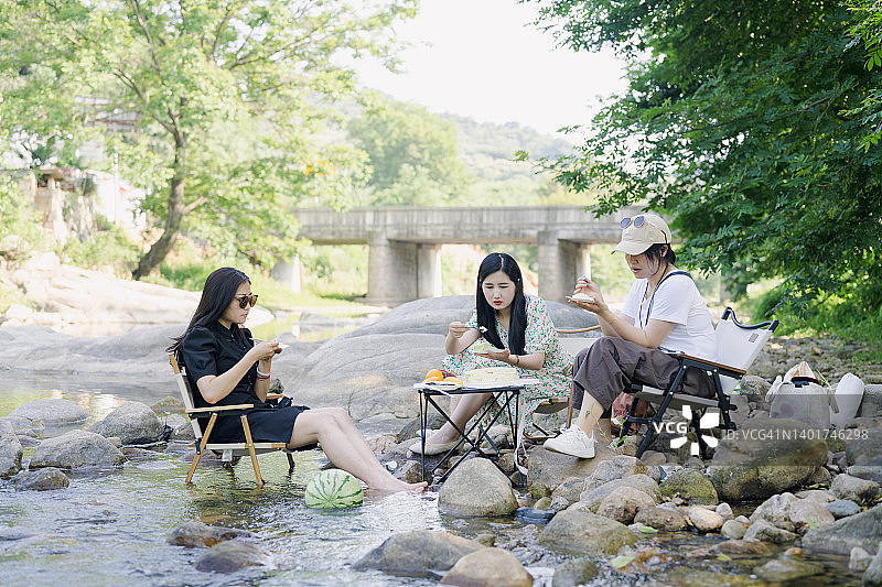 三个年轻女子在河边野餐，品尝糕点，度过了一个美好的夏日周末图片素材