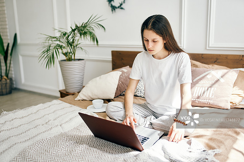 一个轻松的年轻女人在家里使用笔记本电脑。一个年轻的自由职业女性正坐在卧室的床上在线工作图片素材