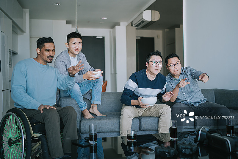 当体育团队赢得冠军时，亚洲男子在家里观看电视上的体育比赛，欢呼庆祝胜利。朋友欢呼,欢呼图片素材