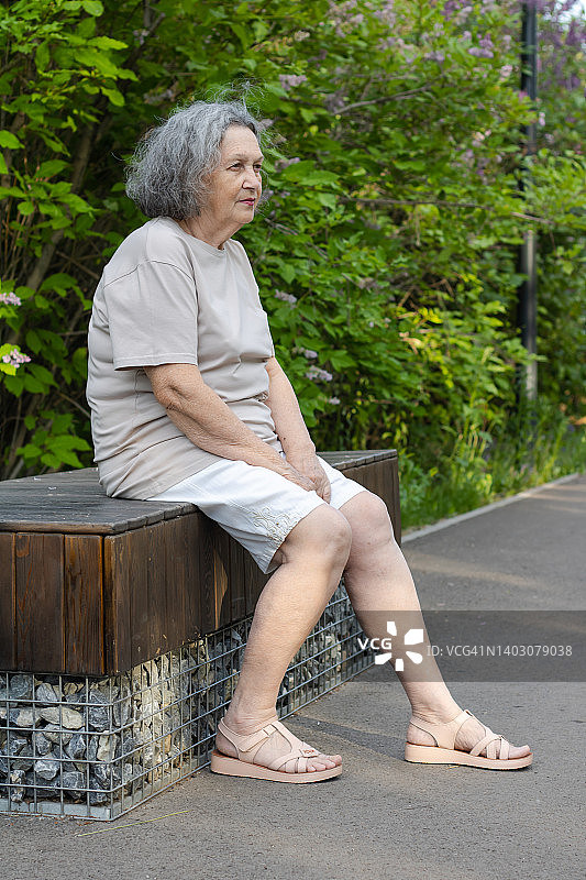 一位老妇人坐在公园的长椅上望着前方图片素材