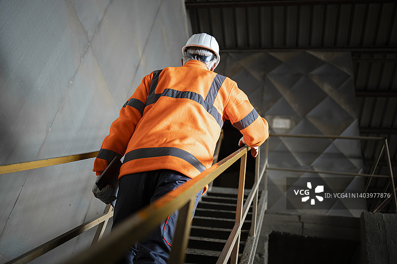 工业工人，安全设备工程师，戴安全帽，在工厂爬金属楼梯。图片素材