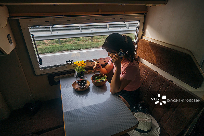 年轻的亚洲女性喜欢在她的面包车里用她的智能手机吃沙拉早餐图片素材