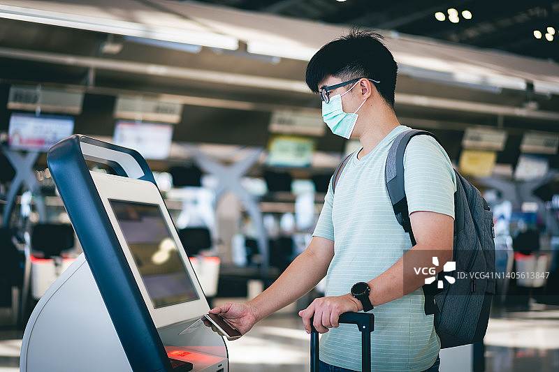 一名亚洲年轻男子戴着防护口罩在机场自动值机图片素材