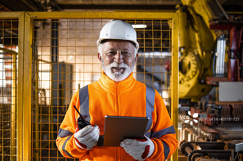 工业工程师专家的肖像，在可见的制服和安全帽站在机器人手臂在制造工厂检查机器的工作流程。图片素材