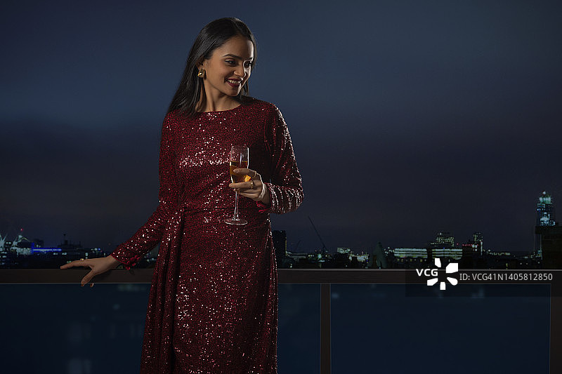 欢快的年轻女子站在阳台上与一杯葡萄酒在屋顶派对图片素材