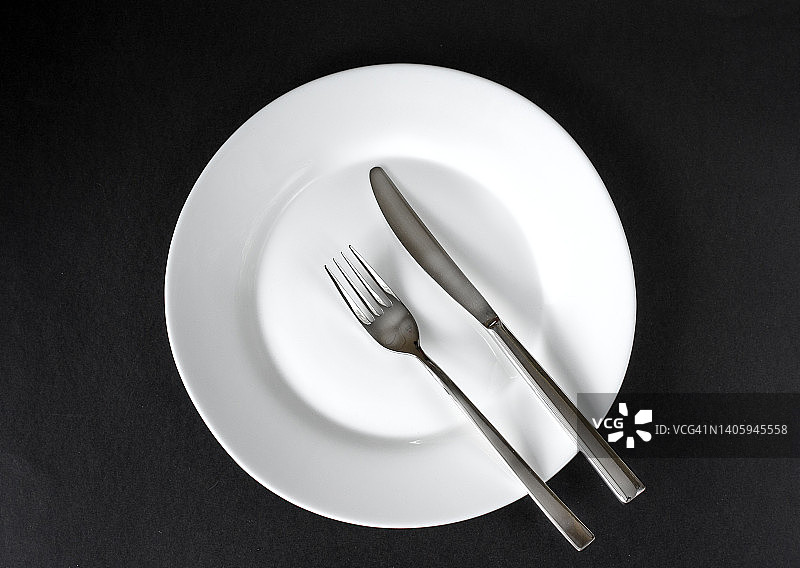 黑色背景上孤立的白色空盘子和不锈钢刀叉。俯视图图片素材