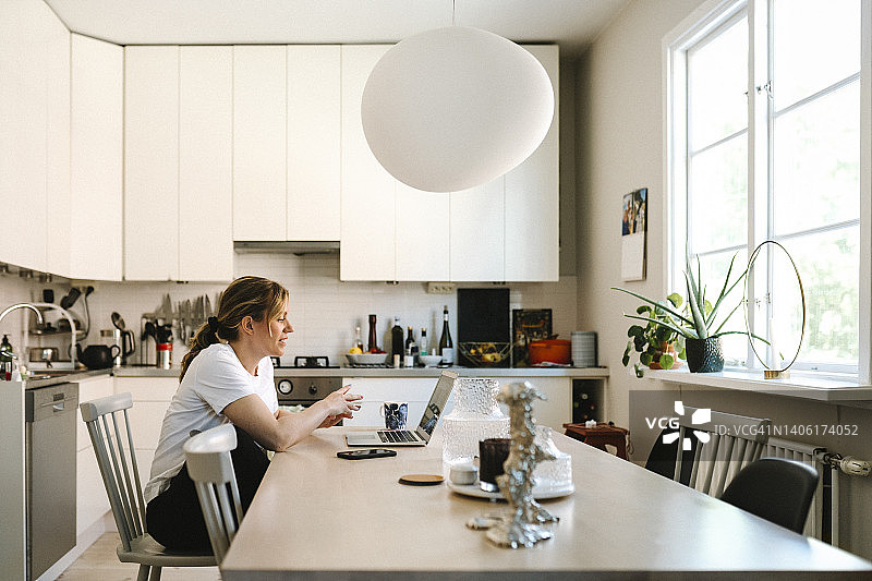 女性自由职业者在家里的厨房通过笔记本电脑进行视频通话图片素材