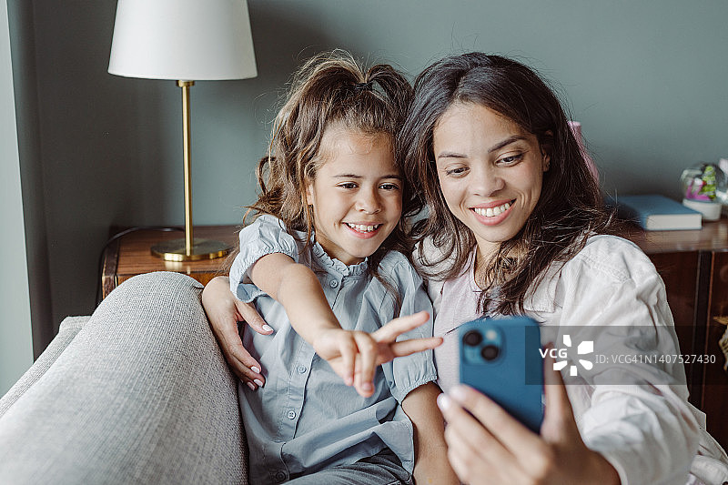 妈妈和微笑的小女儿在家里用智能手机图片素材
