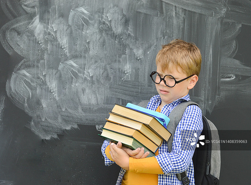 回到学校。心烦意乱的戴眼镜的白人小男孩会思考，还会挠头。一个拿着书和书包的小学生。图片素材
