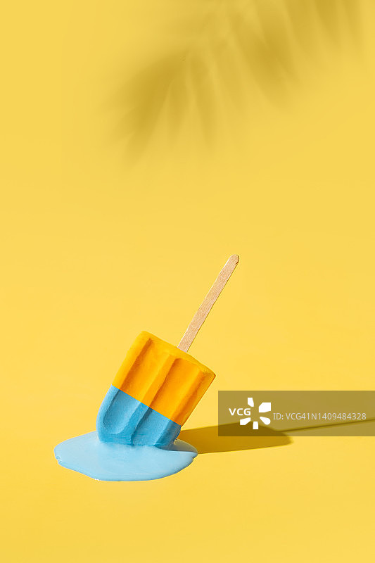 黄色和蓝色的冰淇淋在烈日下融化。棕榈叶的影子。炎热的天气的概念。垂直格式图片素材