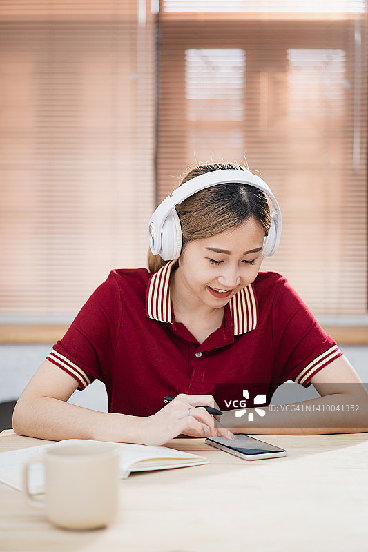 年轻的日本女子坐在客厅里，戴着耳机，在公寓教室里听音频课图片素材
