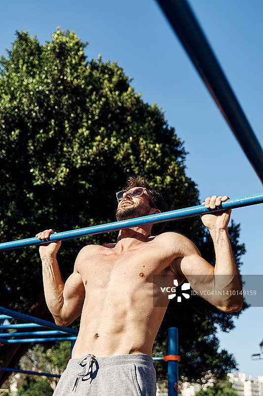 年轻的肌肉男在公园的体操酒吧里做引体向上。图片素材
