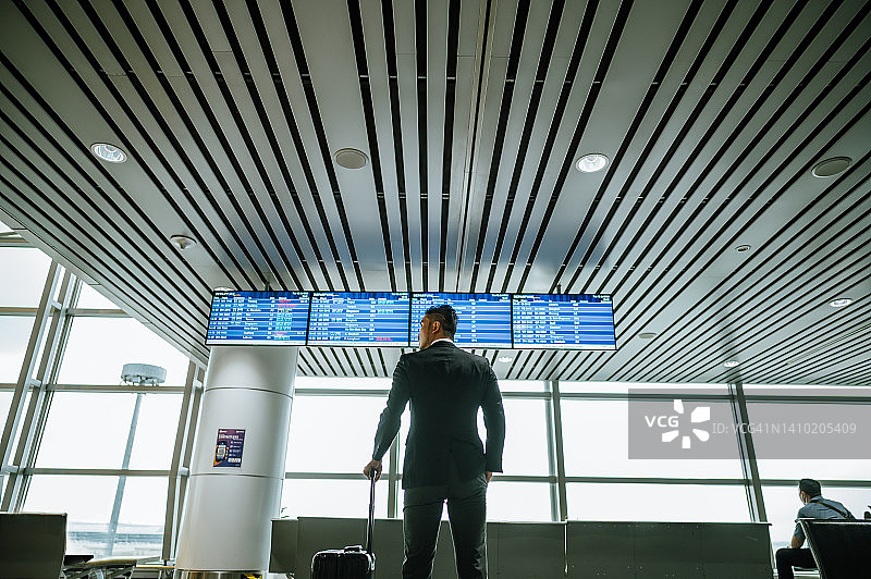 人像后视图的一个亚洲商人站在机场出发区出发板前。图片素材