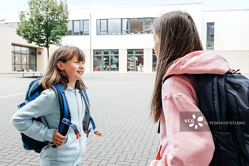 十几岁的女孩背着双肩包在学校的院子里聊天。青少年学童与同龄人的交流。图片素材
