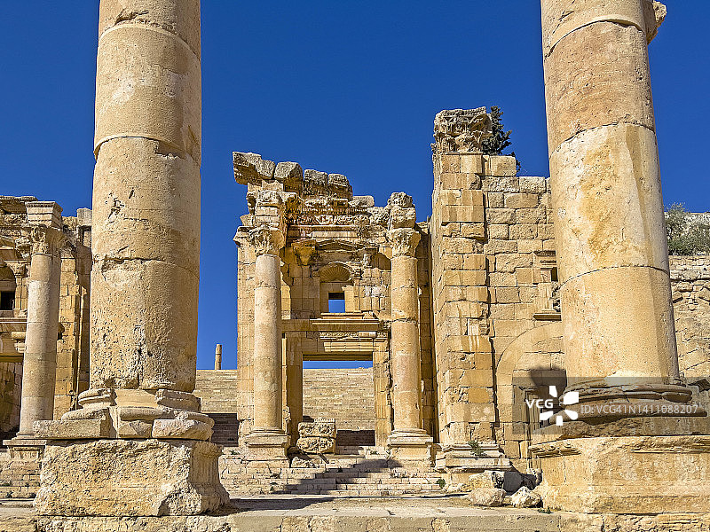 经典的科林斯式圆柱排列在杰拉什罗马遗址中心的石头铺成的街道或车行道上，通往石门。图片素材