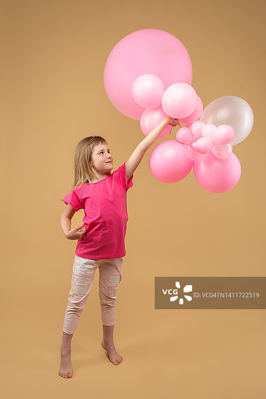 一个快乐的小女孩手里拿着许多粉红色的气球图片素材