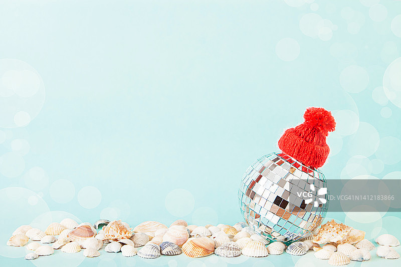 极简创意圣诞艺术构图。镜像圣诞迪斯科球在红色的帽子上贝壳在柔和的蓝色背景。复制空格，文本空格。图片素材