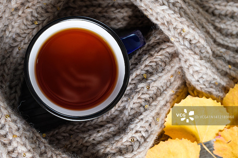 一杯热咖啡或茶，明亮的秋黄树叶，一条温暖舒适的针织羊毛围巾，背景是木制的或桌子。季节性的休息、放松和安心的概念。温暖舒适，爱好手工。文本空间的副本。图片素材