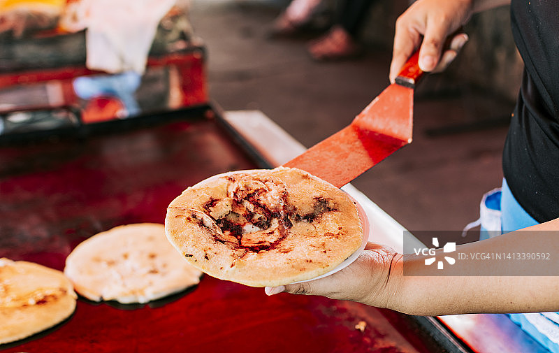 手拿着一个新鲜制成的pupusa在盘子上，传统pupusa服务在盘子上的近距离。传统的萨尔瓦多普普斯奶酪是用融化的奶酪制成的图片素材