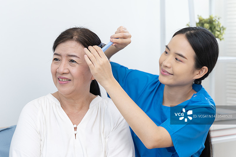 家庭保健亚洲女护士帮助女性老年病人穿衣服。图片素材