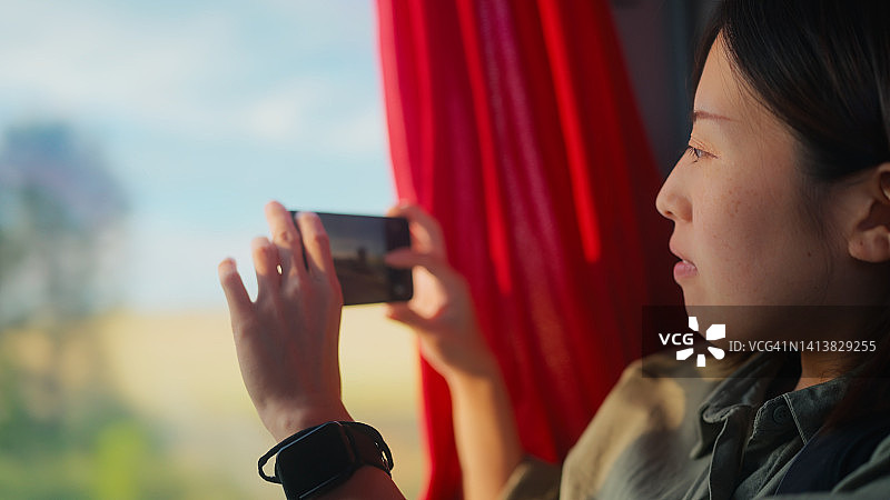 年轻的女游客坐在公交车靠窗的座位上，用手机拍下窗外的风景图片素材