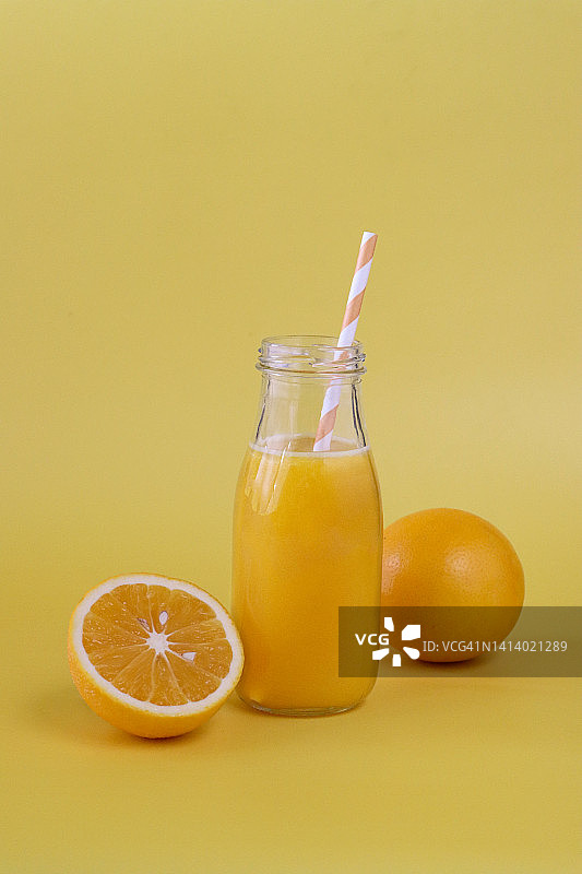 图像的玻璃，螺旋盖瓶橙汁与剥离饮用吸管，整个和一半柑橘水果，黄色的背景，重点在前景图片素材