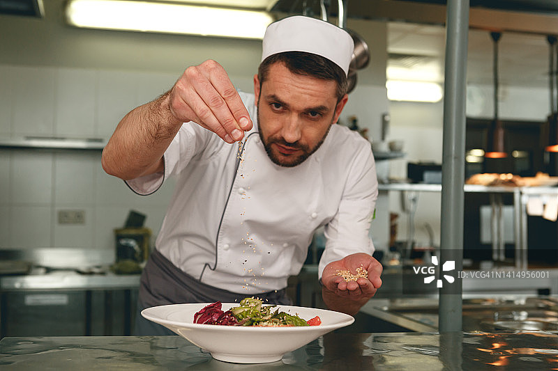 厨师在餐厅厨房的新鲜蔬菜沙拉上撒盐。美味健康的食物图片素材