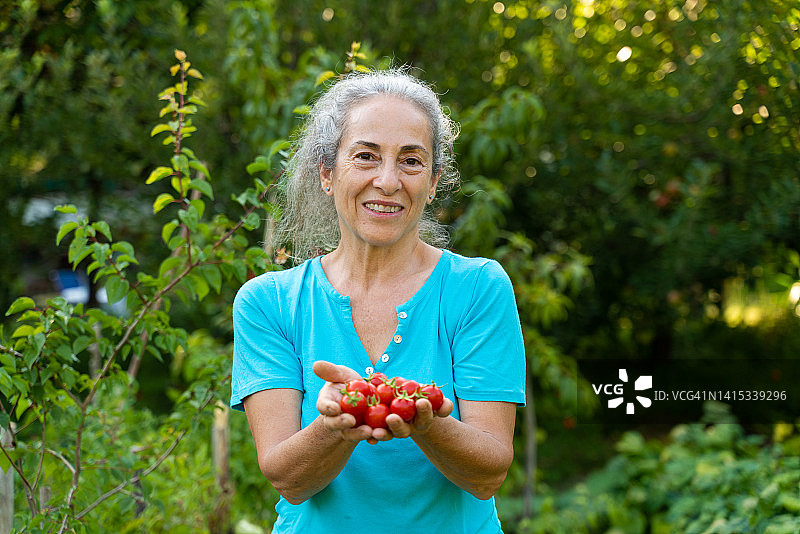 老妇人拿着自家种的蔬菜篮子，在花园里看着镜头图片素材