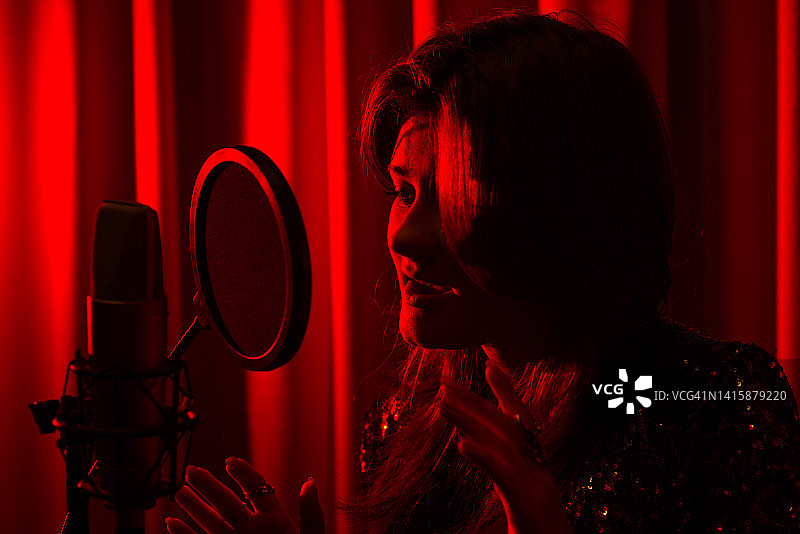 特写情绪化的年轻女子歌手唱歌和录音歌曲在录音棚的红色灯光发光的背景图片素材