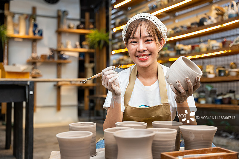 年轻的亚洲女艺术家在陶艺工作室制作手工陶瓷杯图片素材