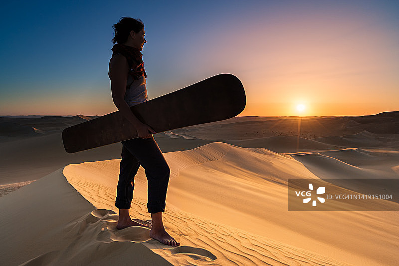 一名年轻女子在非洲撒哈拉沙漠日落时玩沙板图片素材