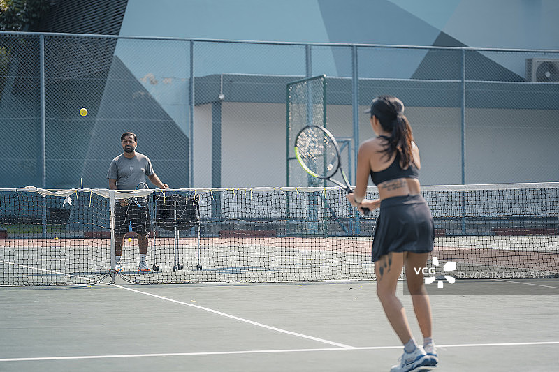 亚洲中国女网球运动员在周末的早上和她的教练在硬地场上练习图片素材