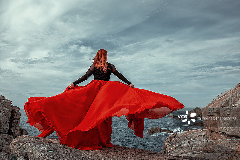 红裙子和红头发的女人在岩石上摆姿势图片素材