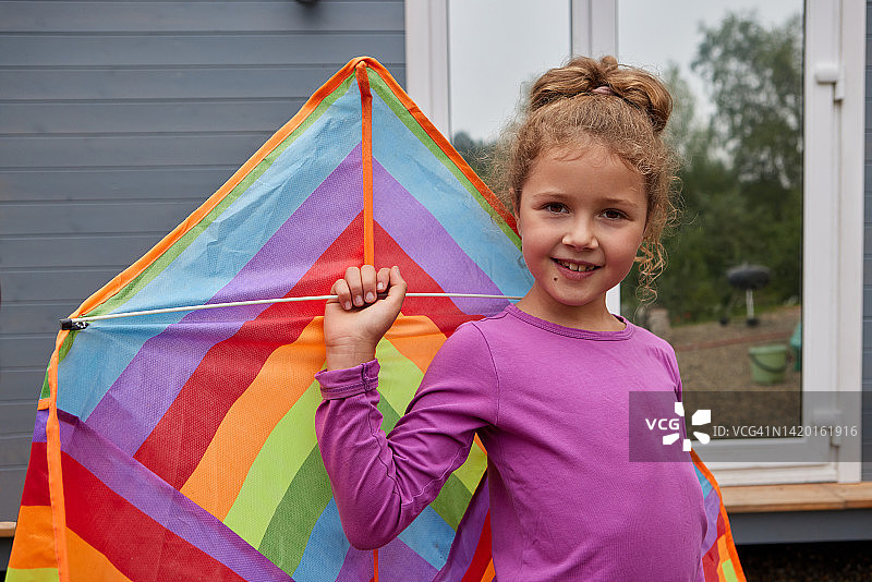 女孩微笑着躺在草地上，拿着五颜六色的彩虹风筝玩具。快乐的童年时光或户外时光的概念形象。图片素材