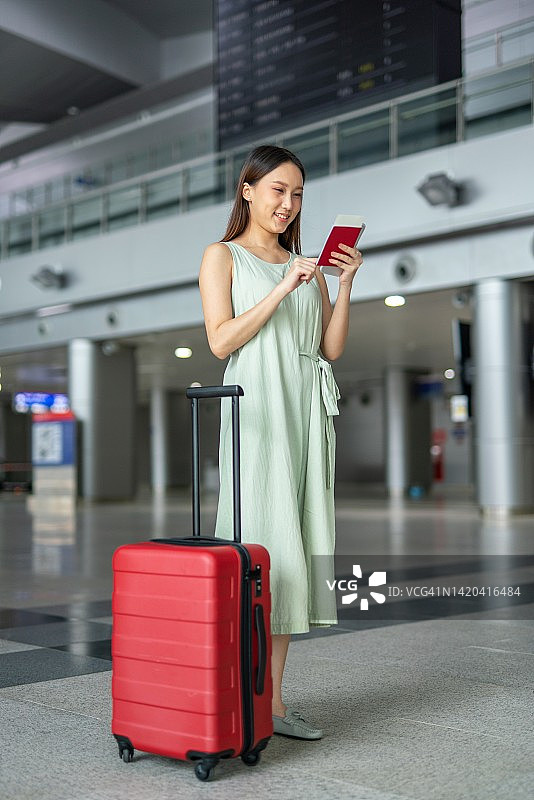 一个年轻的亚洲女性的肖像照片与她的手机和行李箱走过一个出发板去她的梦想的度假目的地旅行图片素材