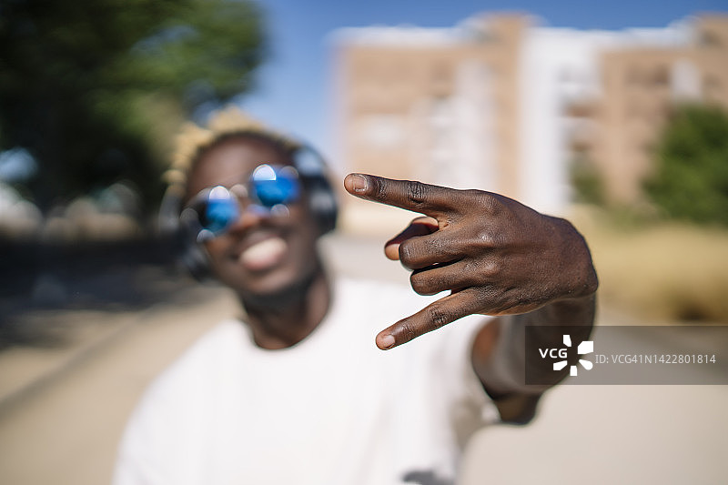 时尚的非洲男人戴着墨镜，戴着耳机听音乐，做手势图片素材