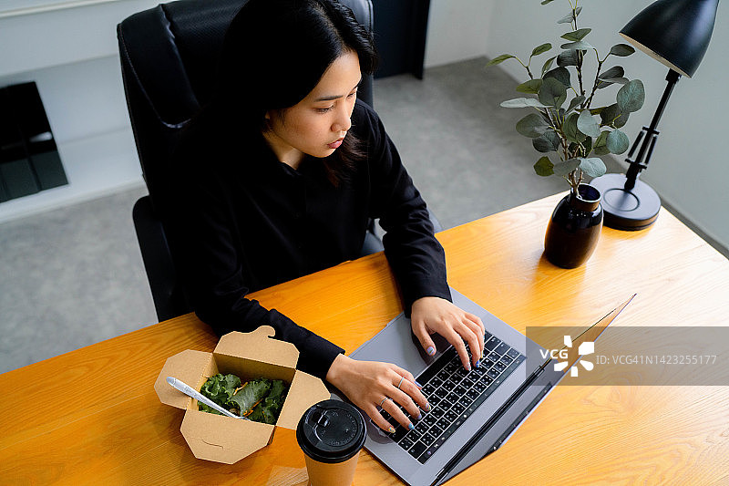 亚洲女性工作人员在电子平板电脑上工作，吃着健康的饭菜。图片素材