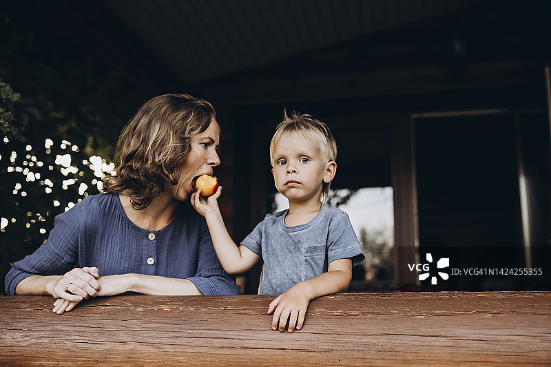 小男孩在阳台的木栏杆旁给妈妈喂水果图片素材