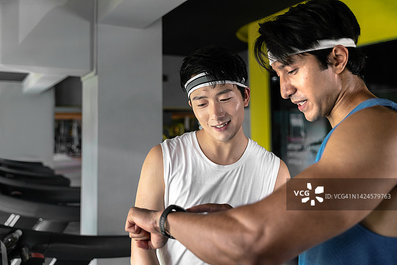 亚洲年轻人在健身房的跑步机上跑步或慢跑的侧视图。图片素材