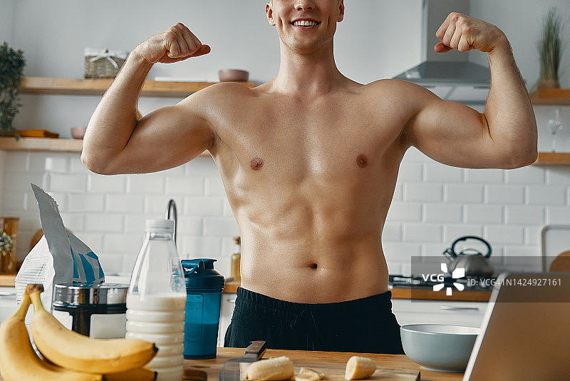 面目全非的健康男子在厨房里准备健康食品时露出了他的肱二头肌和微笑图片素材