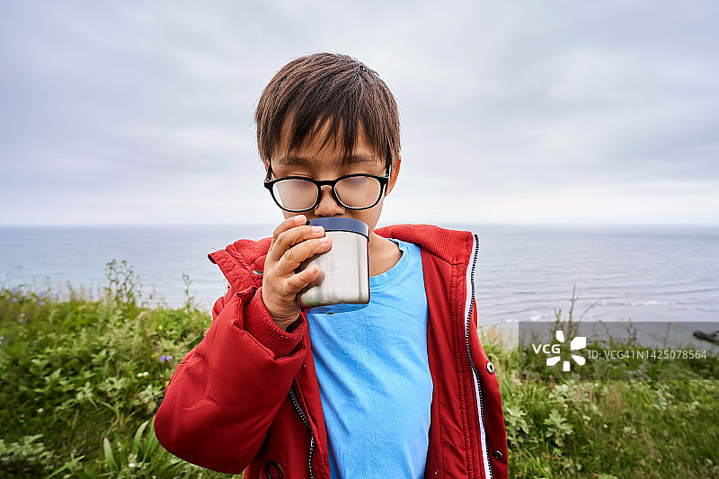 一个戴着雾状眼镜的男孩正在山顶上喝茶。图片素材