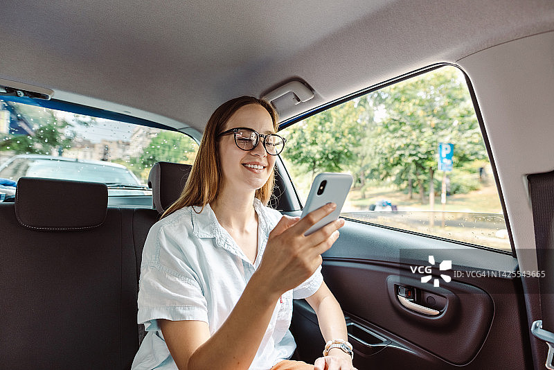 一名年轻女子在出租车后座使用智能手机图片素材