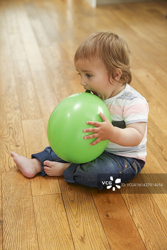 小男孩叼着气球躺在硬木地板上图片素材