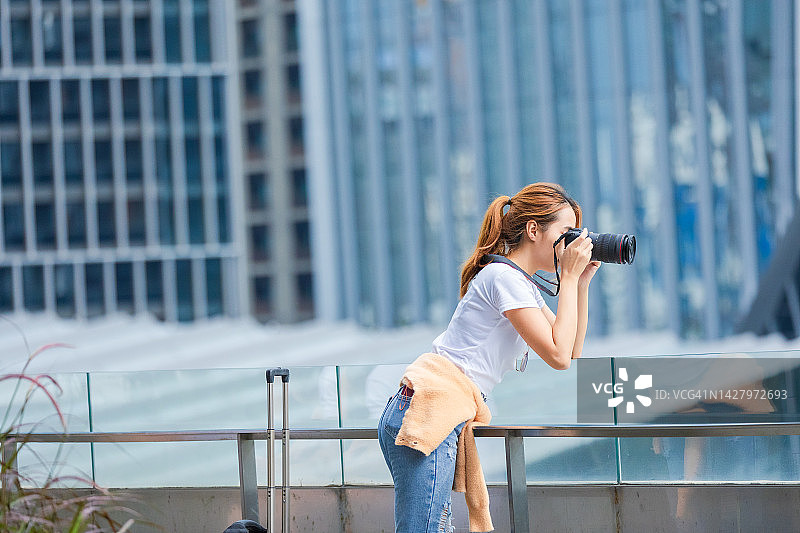 亚洲妇女在城市里用相机拍照。图片素材